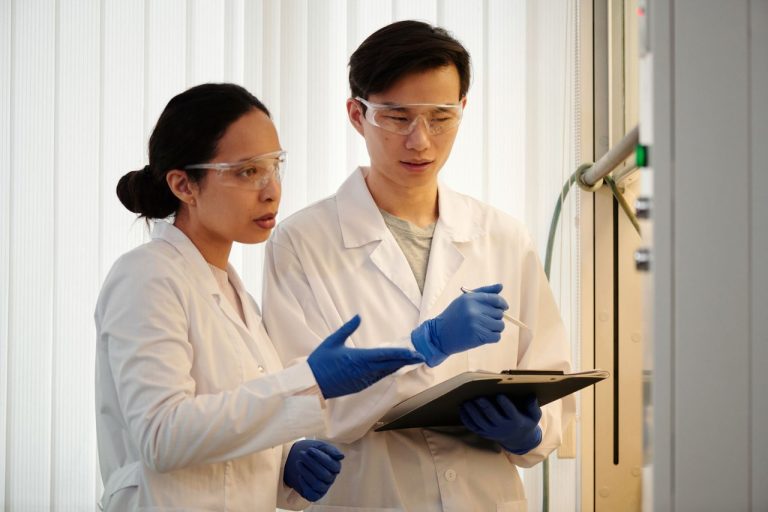 Fazenda anuncia medidas para preservar recursos destinados à pesquisa científica Pesquisadores usando equipamentos de proteção e luvas azuis analisam dados em um laboratório.