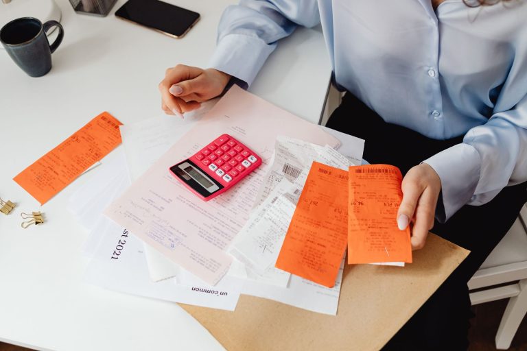 Desenrola Brasil 3.0 amplia renegociação de dívidas para pessoas físicas Mulher analisa recibos e calcula despesas com uma calculadora em uma mesa de trabalho.