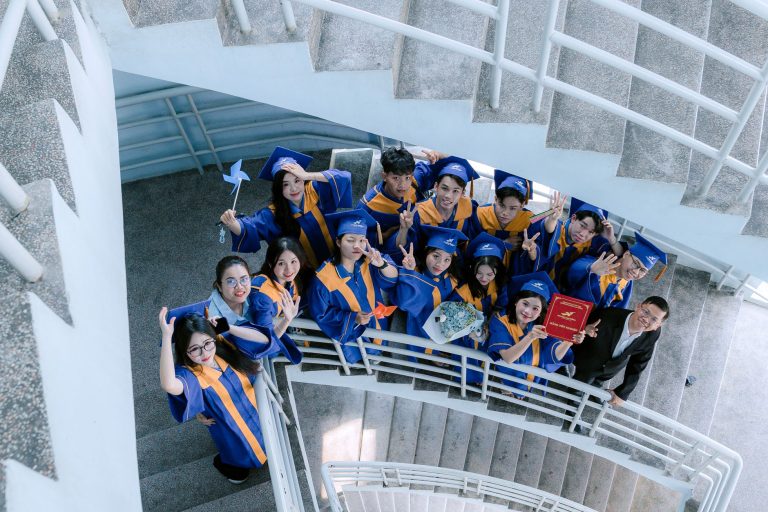 Grupo de formandos usando becas azuis celebra em uma escadaria durante uma cerimônia de formatura.